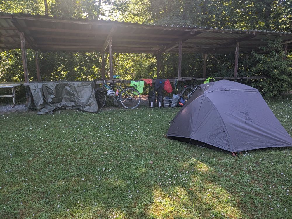 A gray tent is in the foreground and in the background there is a long roofed area that has many things hanging off it. 
