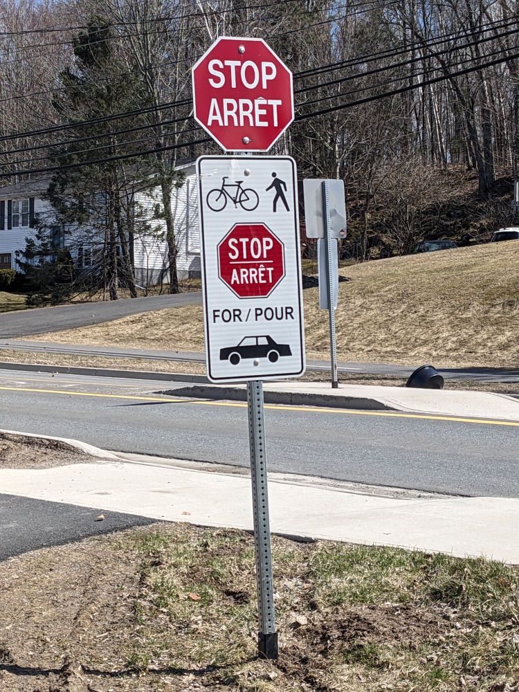 A stop sign on a trail that explicitly says bikes and pedestrians stop for cars.