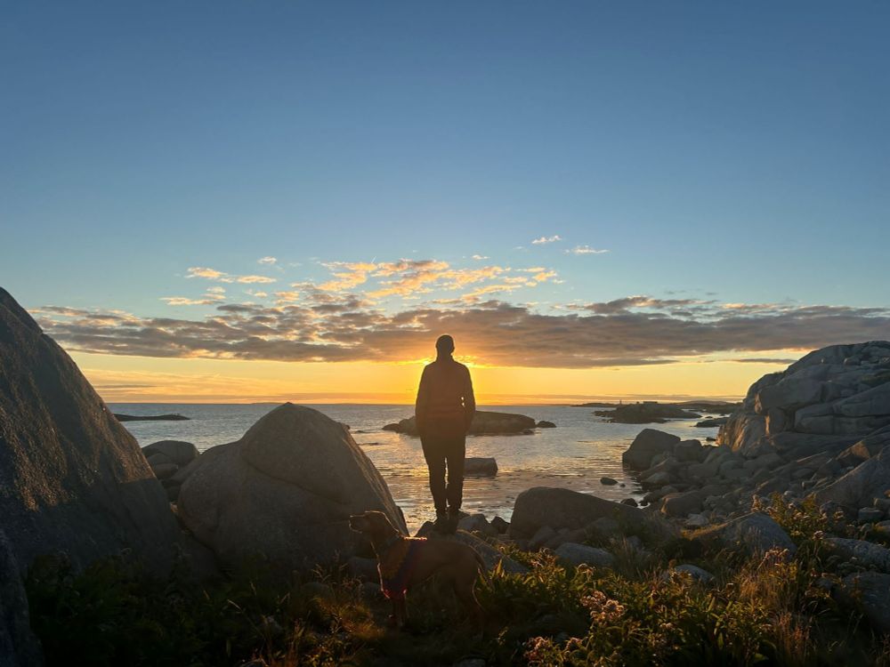 The silhouette of a person standing on a rock watching a sunset. The person is perfectly blocking the sun.
