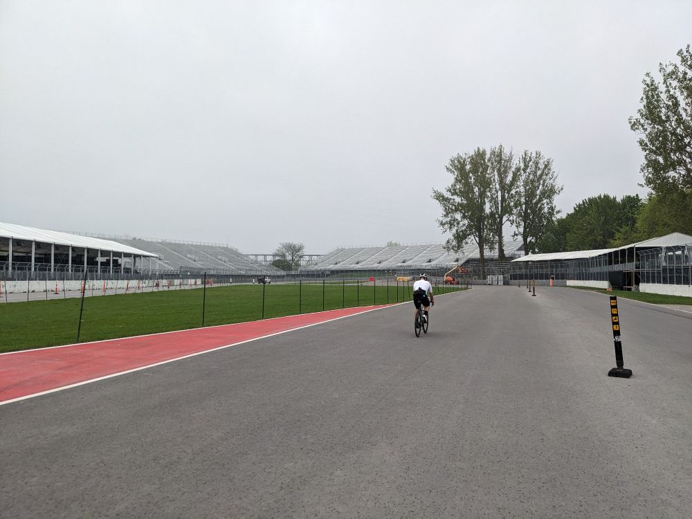 A cyclist riding on a wide road with grandstands on either side. There could be flames out the back of his bike because he was riding so fast past me. 