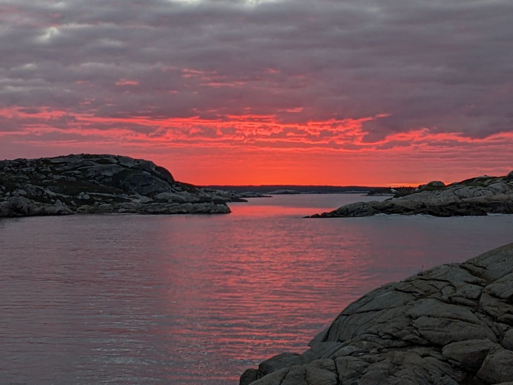 A pink sunrise over a Cove with large rocks on either side.