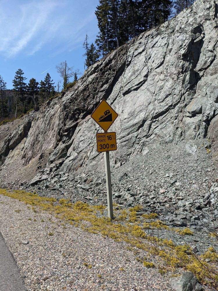 A sign showing a car and a trailer going downhill. THe sign indicates a 16% grade in 300m.