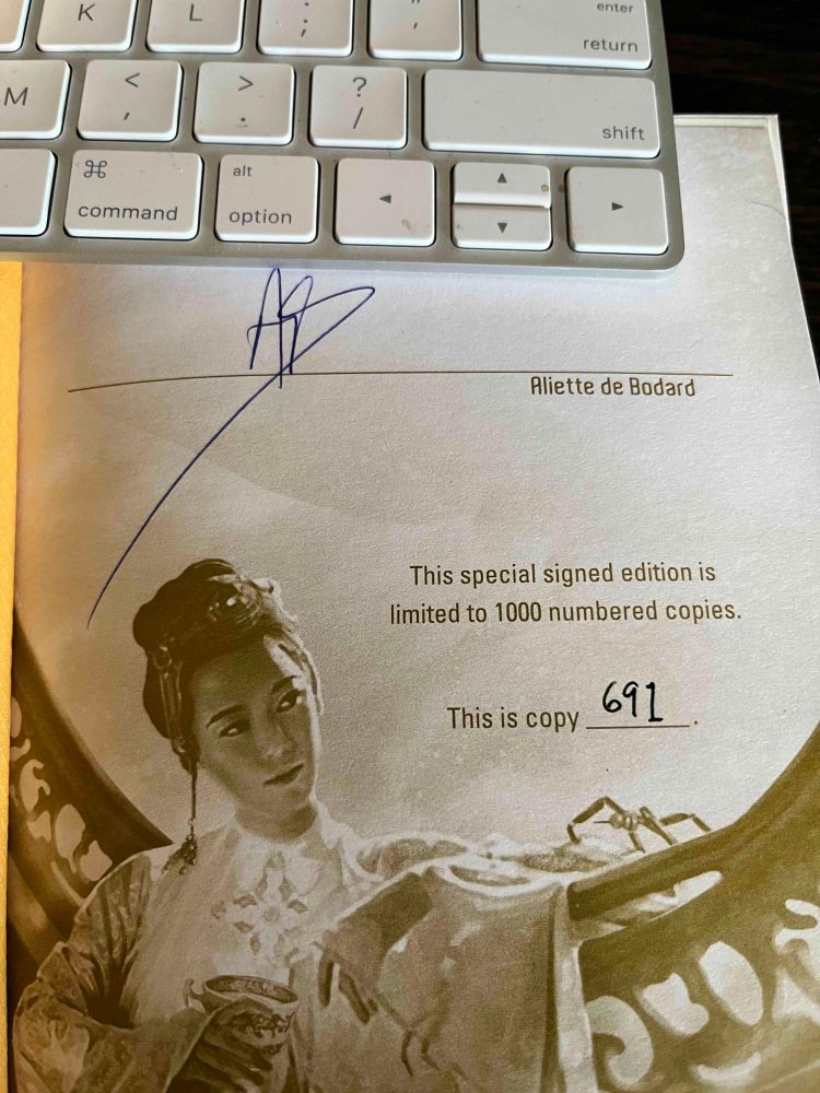 Signed insert sheet. Signature is by Aliette de Bodard and the text reads, "This special signed edition is limited to 1000 numbered copies. This is copy 691." Accompanying image of a woman in silk robes leaning on a curved frame and holding a goblet. 