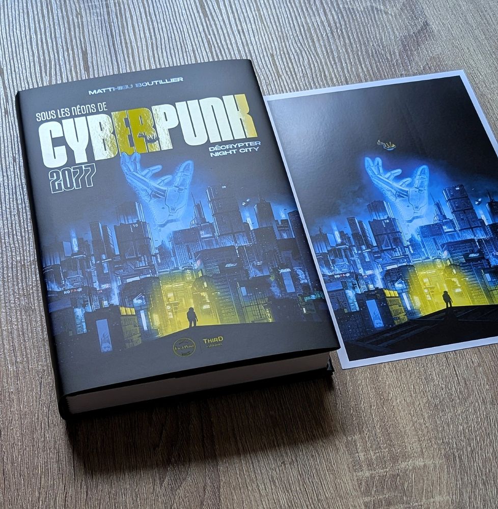 Photo présentant un livre et un tirage de l'illustration de couverture du livre. Le livre s'intitule Sous Les Néons de Cyberpunk 2077 - Décrypter Night City, et a été écrit par Matthieu Boutillier et édité par Third Editions.
Sur la couverture on voit une illustration de la ville futuriste du jeu vidéo occupant la grande majorité de la couverture. L'illustration sur fond de nuit, très sombre, est éclairée par les lumières, hologrammes et  néons de la ville.