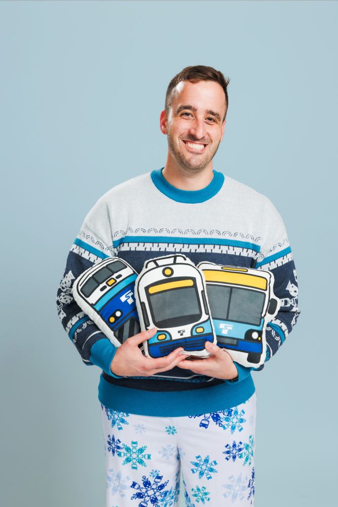 A person holding limited edition plush trains and wearing the matching snowflake sweater and pajama pants.