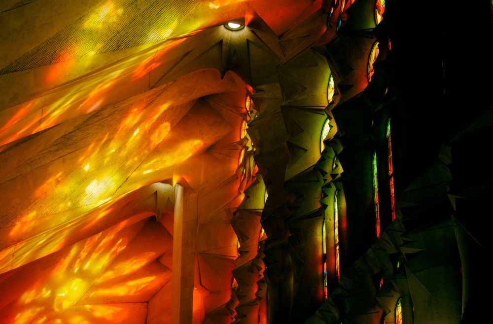 Interior de la Sagrada Familia en Barcelona. La luz que entra por los ventanales se refleja en el techo de la basílica en tonos amarillos y rojos.