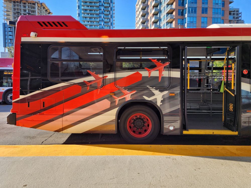 Decals of planes adorn the rear half of a Toronto Transit Commission Airport Express bus, while doors welcome passengers travelling from Kipling Station to Pearson International.