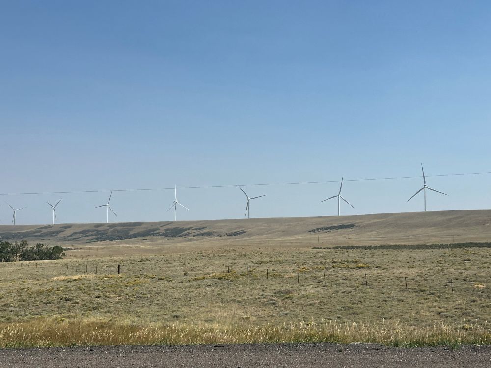 An empty prairie with seven visible wind turbines visible on the horizon. From a distance and with a little imagination and a sick sense of humor, you can imagine they are a line of crucifixes.