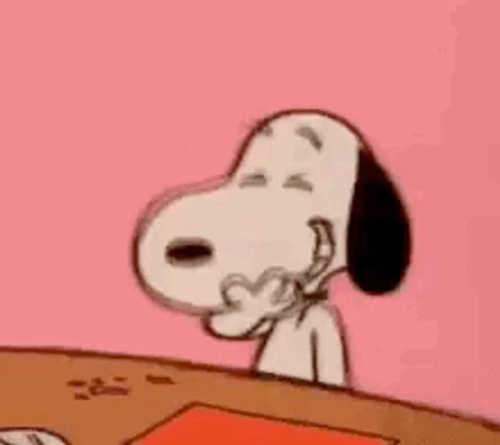 snoopy is sitting at a table with his eyes closed and his hand in his mouth .