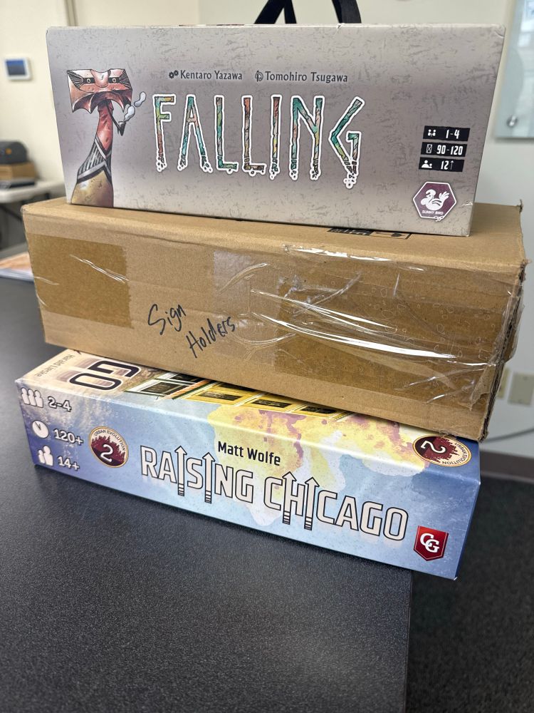 Box with sign holders written on side and board game boxes for FALLING and Raising Chicago