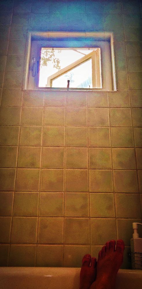 picture taken from the tub, pointing at my feet, at the other end, with a background of greenish tile and a square window up above