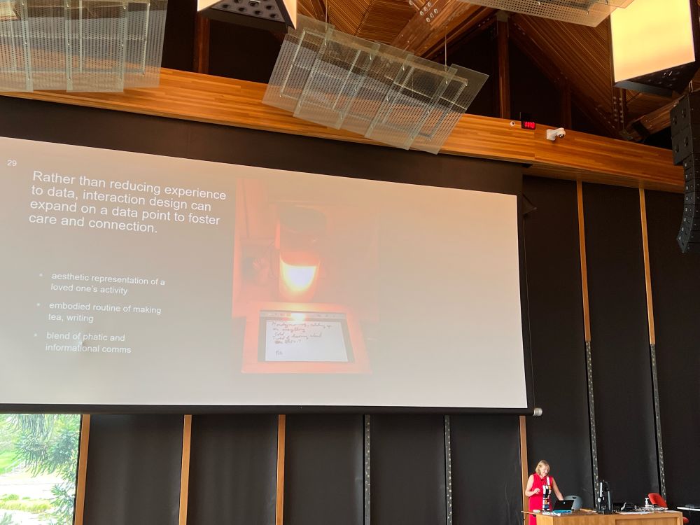 Photo of a speaker presenting at a lectern with a slide in the background 