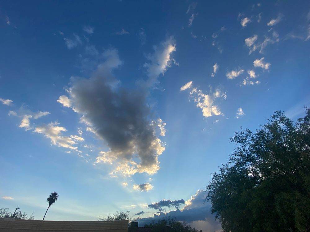 a photo of sun rays illuminating a large cloud formation nearing sunset