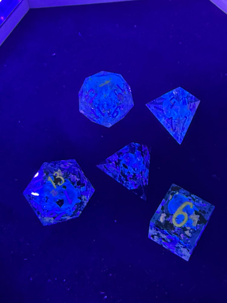 Assorted dice in blacklight rolling tray, showing vague shapes inside because I take terrible photos. Silver numbers glow pink.