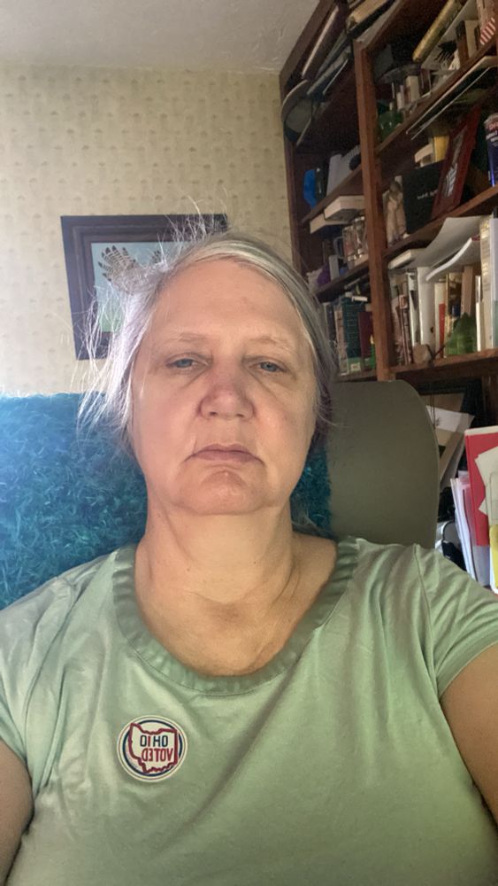 Woman frowning into camera, with Ohio Voted sticker prominently displayed on green shirt.