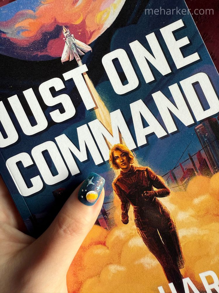 Features the book "Just One Command" by M.E. Harker. Overtop the book is a hand holding it, with a thumb nail painted with a space-themed design.