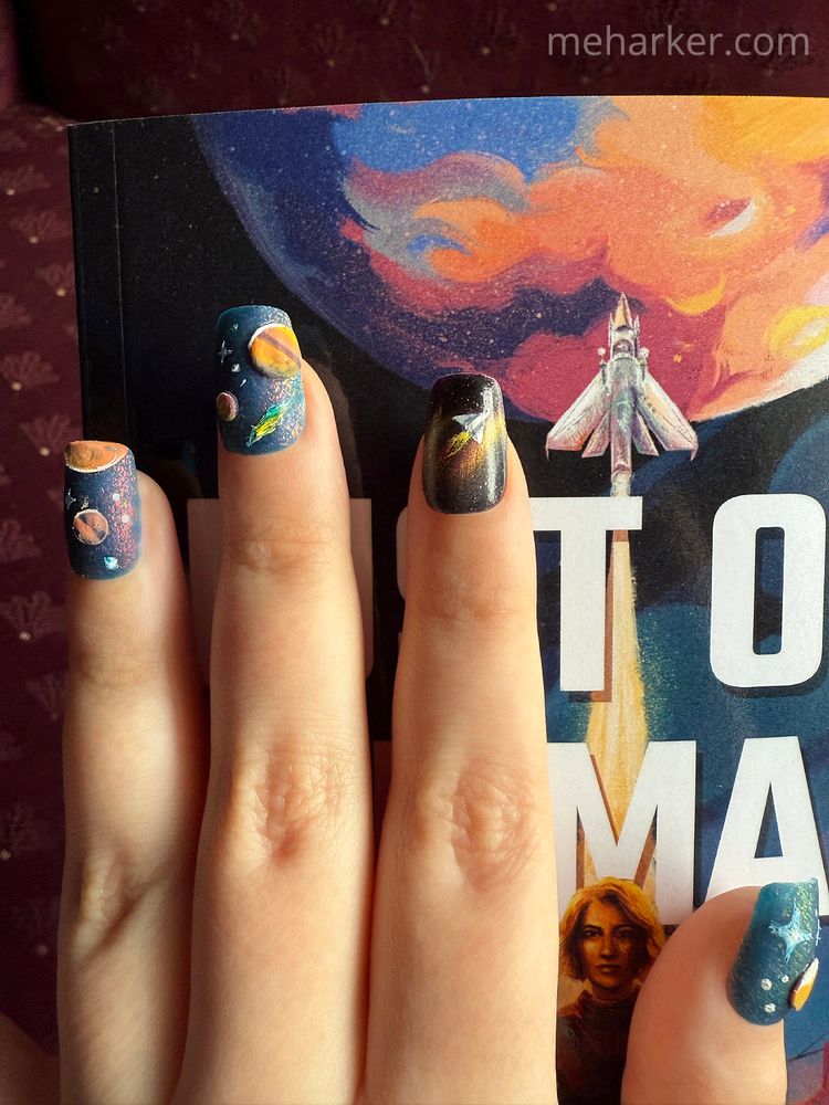 An index finger with a rocket-ship themed nail polish design on it sits on top of a book. The book has a similar rocket ship on its cover.
