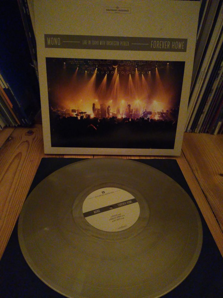 Cover der LP Forever Home von Mono, Cover zeigt hell erleuchtetes Bühnenbild (Band mit Orchester)