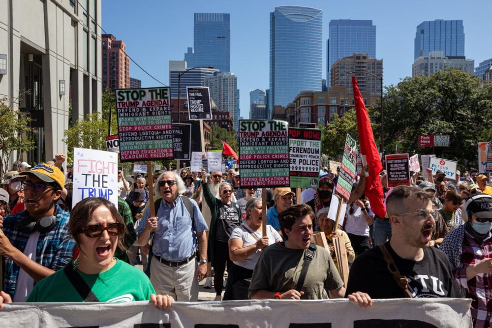Protestors march behind a banner holding Coalition Against the Trump Agenda signs with the Chicago skyline in the background
