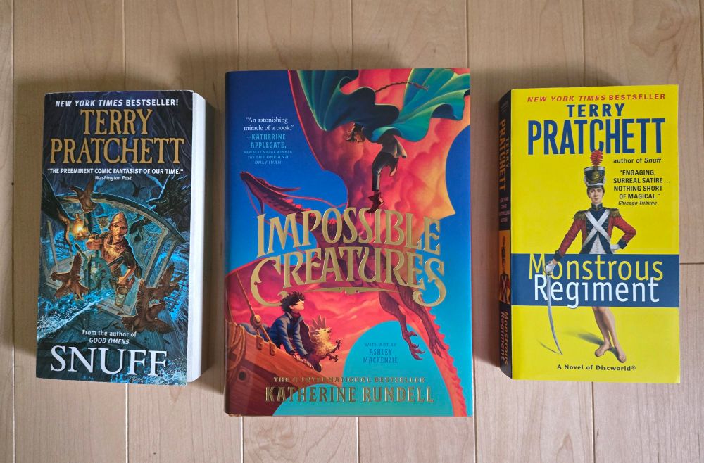 Three books side by side: Snuff by Terry Pratchett, Impossible Creatures by Katherine Rundell, and Monstrous Regiment by Terry Pratchett