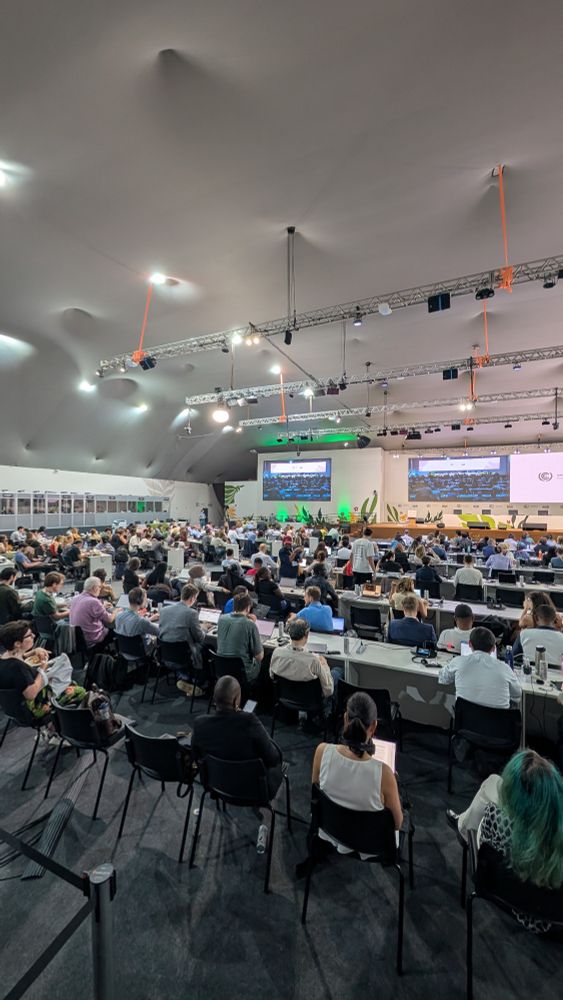 Menschen sitzen in einem großen Konferenzraum vor einer Leinwand 