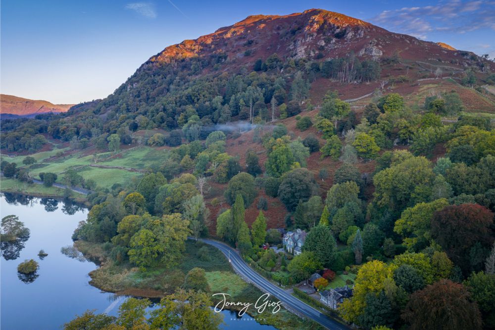 Drone shot over Rydal Water showing the A591 as the early sunrise starts to hit the Lake District fells. 