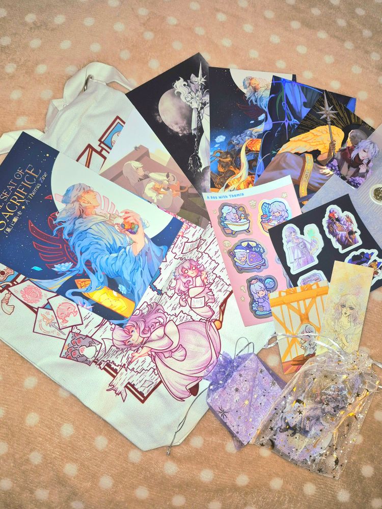 A volume of the Themis zine and all of its merch (a tote bag, several prints, sticker sheets, a standee, a bookmark, memo pad,  and keychains).