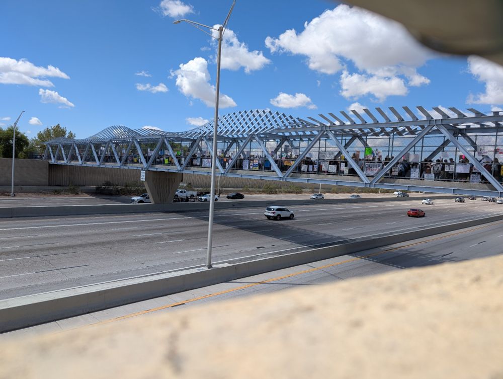 Protesters atop a pedestrian bridge over a busy freeway (US-60) holding pro-democracy signs.