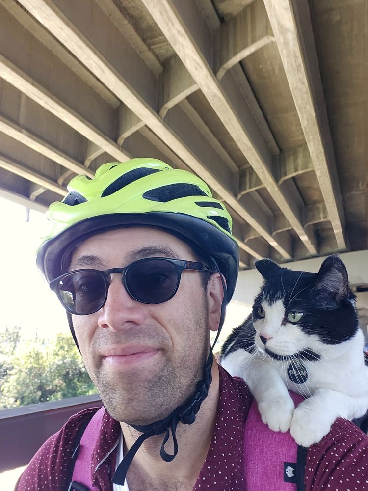 It's me! A dude with a gorgeous black and white cat on his shoulder. While he's biking.