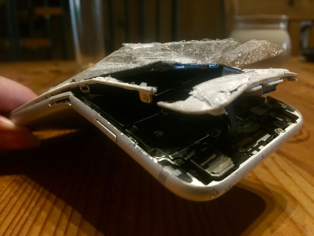 Komplett zerstörtes Mobiltelefon. In mehreren aufgefächerten Schichten dir Rückseite, Rahmen und Glas