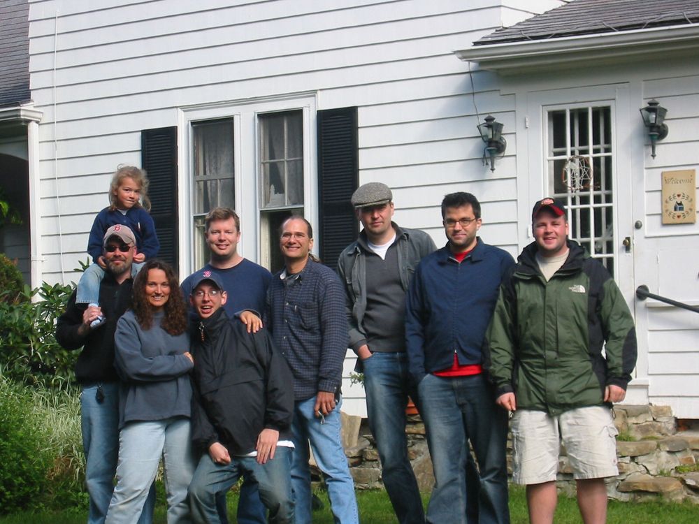 A group of people posing in front of an old white house 