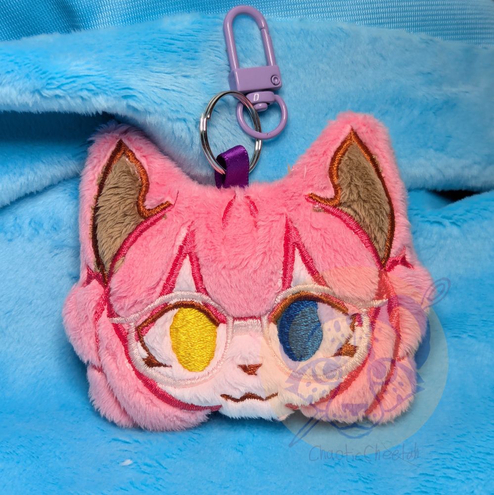 Plush charm artfight attack for justsomegoth. Pink character with pink hair, cat ears, and glasses. 