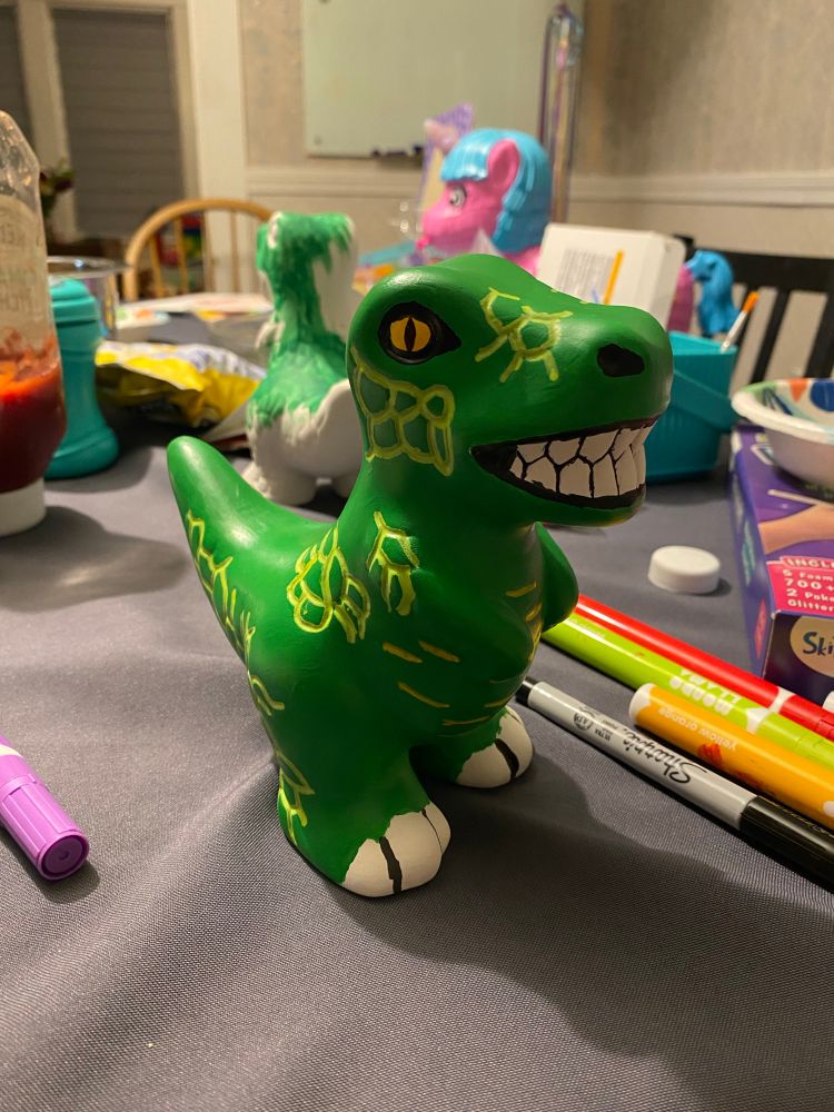 A ceramic dinosaur painted green with light green accents. It was painted by an adult who is not particularly skilled at art but enjoys doing it anyway. 