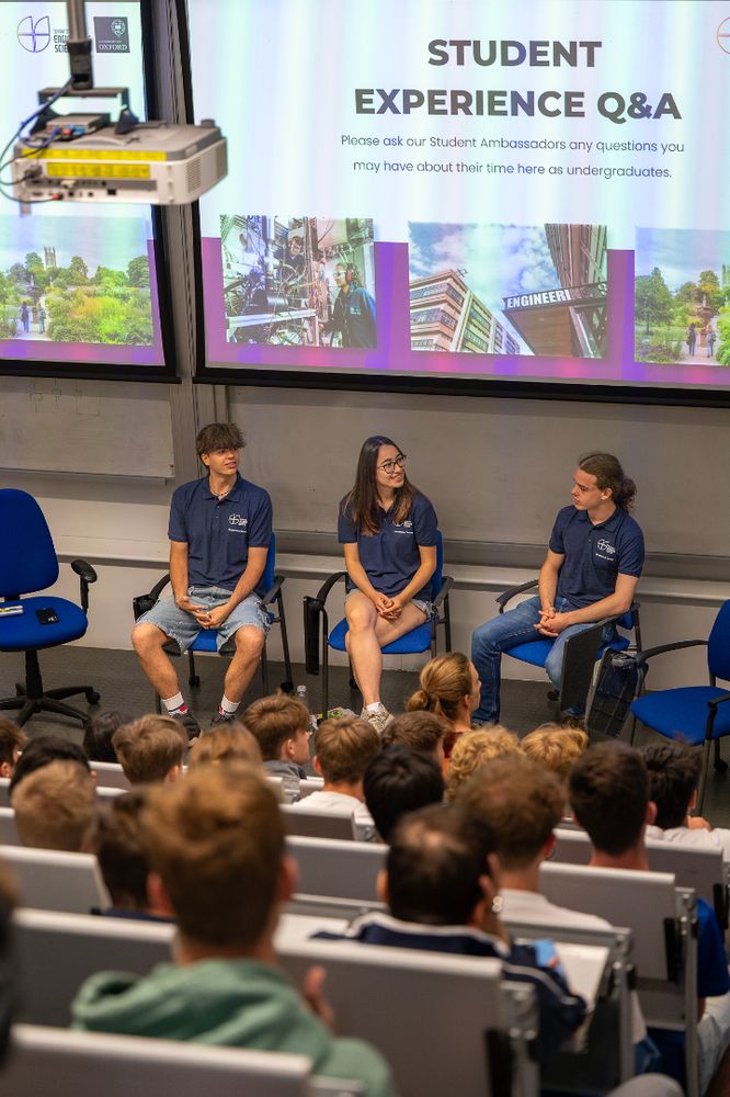 Three student ambassadors sit at the front of a lecture theatre, participating in a Student Experience Q&A session with a large audience of prospective students.