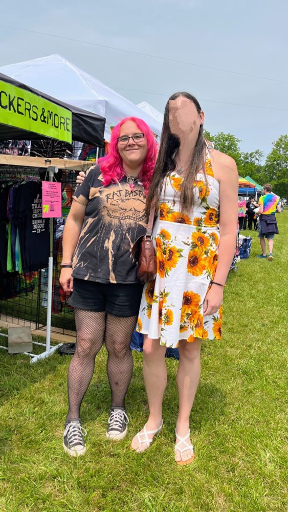 Two women one with pink hair and one with brown hair standing next to each other in an open air market 