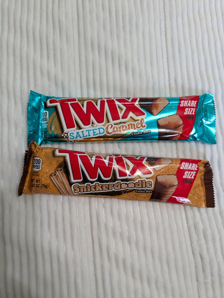 A blue label twix candy bar that says salted caramel on top.
A tan label twix candy bar that says snickerdoodle on the bottom. 