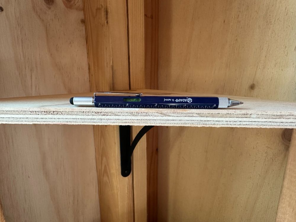 Multi-tool pen being used to level a shelf in a shed