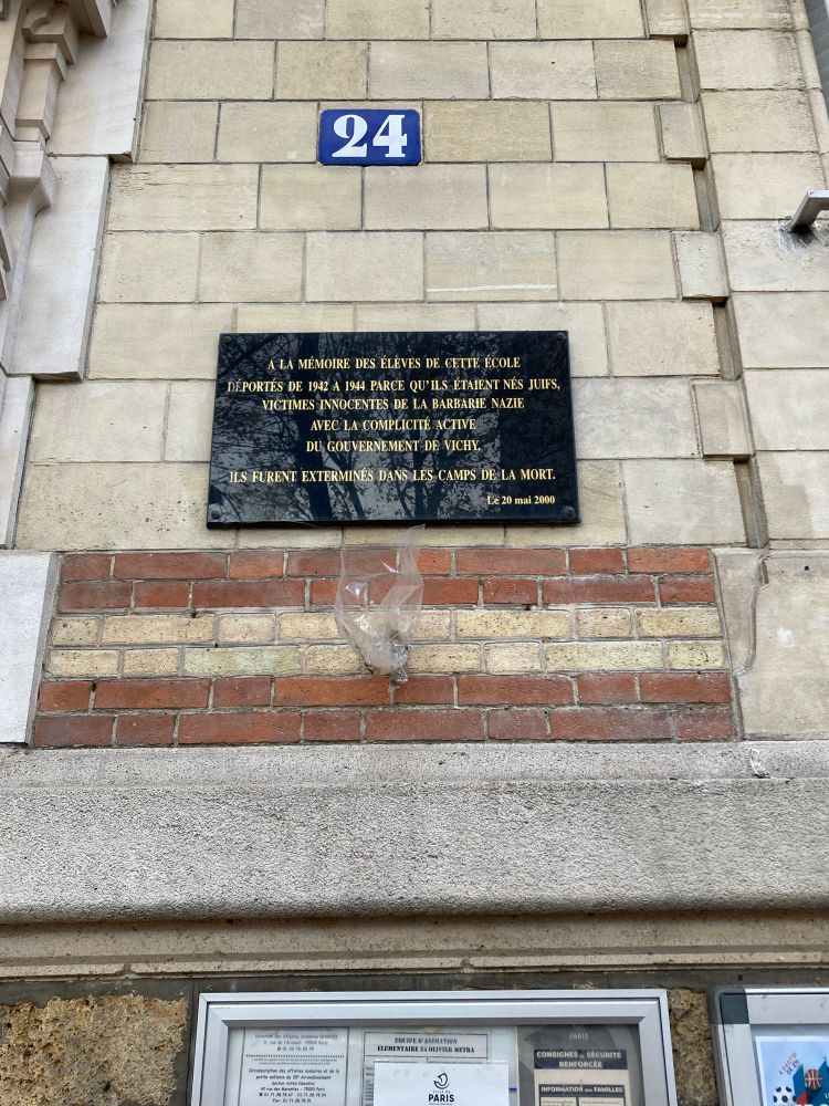 Schwarze Gedenktafel auf gepflasterten Mauer. Oben Zahl 24. Unten ein Teil einer Infotafel. Text : ALA MÉMOIRE DES ÉLÈVES DE CETTE ÉCOLE
DÉPORTÉS DE I94Z A 1941 PARCE QU*ILS ETAIENT NÉS JUIFS,
-VICTIMES INNOCENTES DE LA BARBARIE NAZIE
AVEC LA COMPLICITE ACTIVE
DU GOUVERNEMENT DE VICHY.
ILS FURENT EXTERMINES DANS LES CAMPS DE LA MORT.