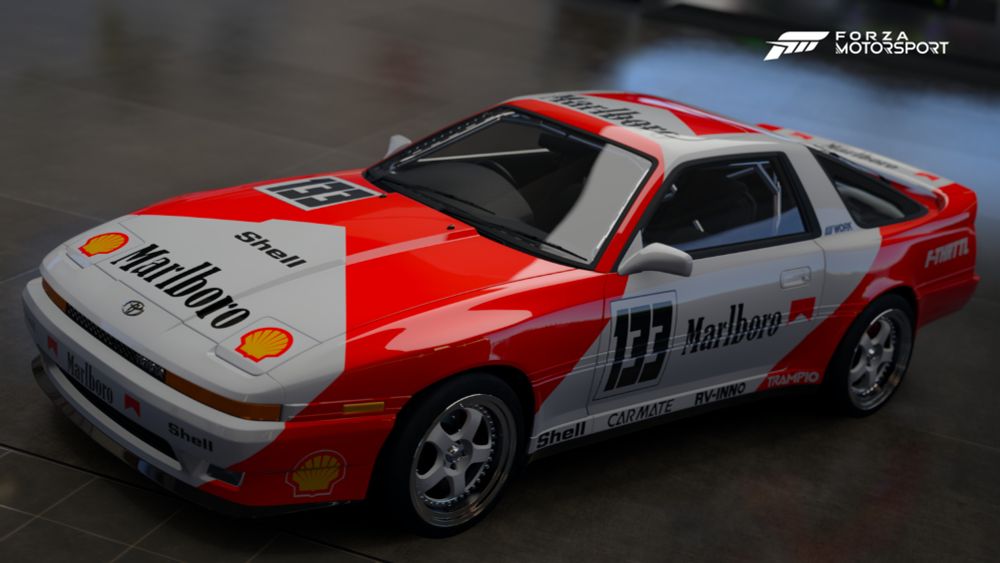 The front 3/4s of an A70 Supra with a wide body and a Marlboro livery in the main garage space on Forza Motorsport 2023