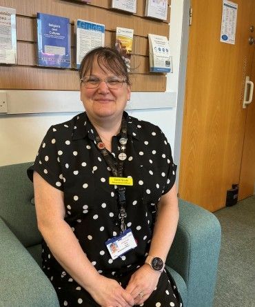 Carol sitting on a chair in front of a display of leaflets about bereavement.