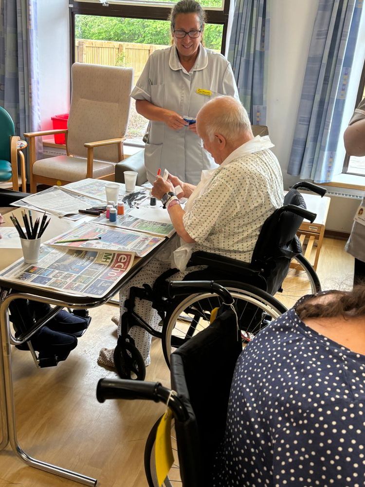 A patient using art supplies while a healthcare professional watches and assists.