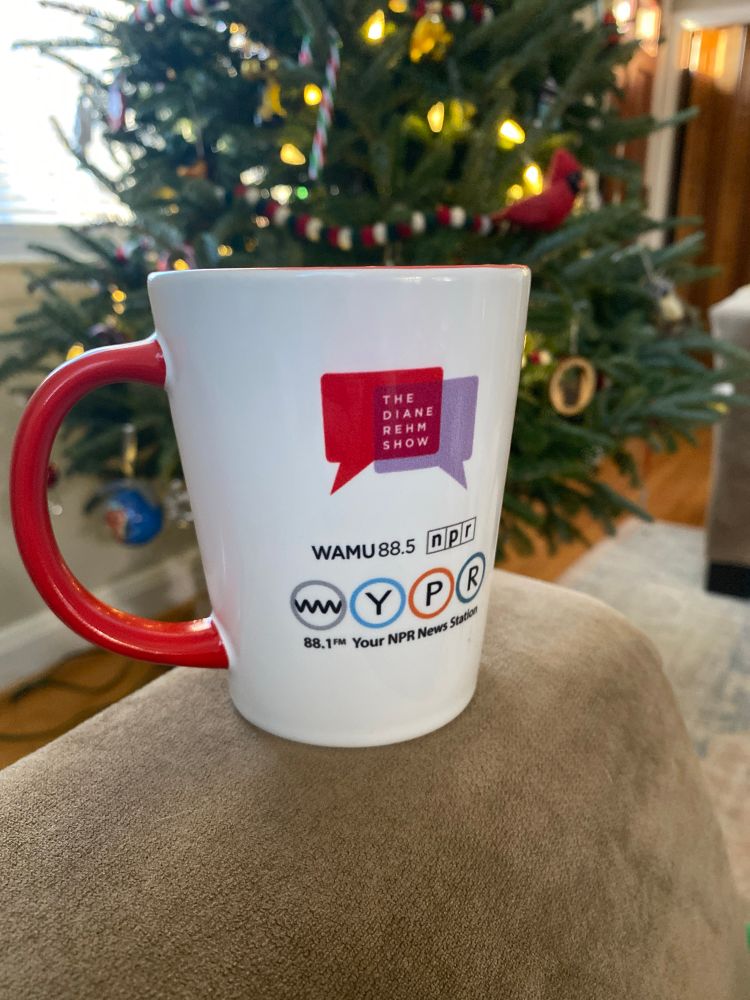 Photo of a WAMU NPR coffee mug balancing on the arm of a tan sofa,
with an out-of-focus Christmas tree in the background.
