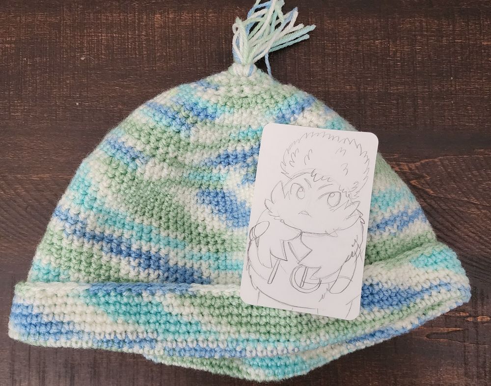 Picture of a nice knit beanie with winter colors and a tassel along with a card sketch of Riki from Xenoblade 3.