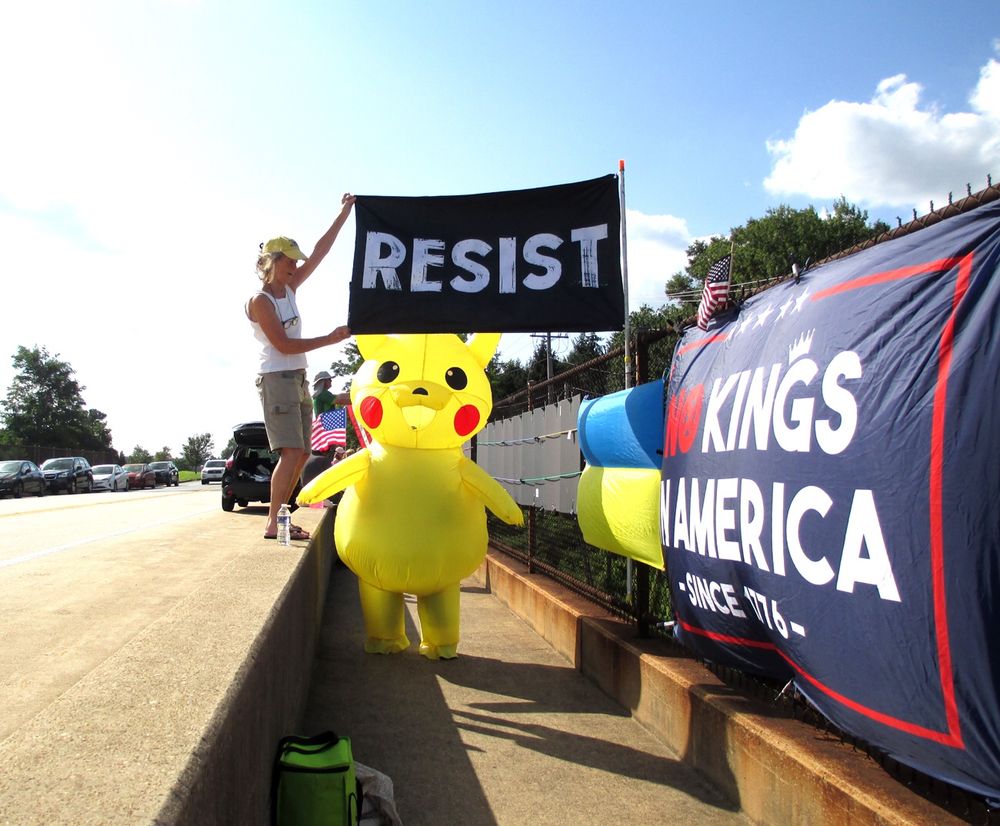 Overpass protest with giant “Resist” and “No Kings in America” flags and a Pikachu. 