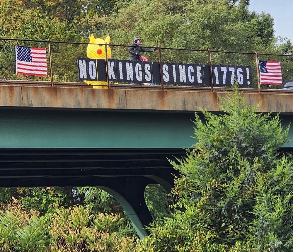 Gorman Rd overpass over I-95 in North Laurel, MD on No Kings, 10/18 with a Pikachu, American flags, and a large letter NO KINGS SINCE 1776! sign. 