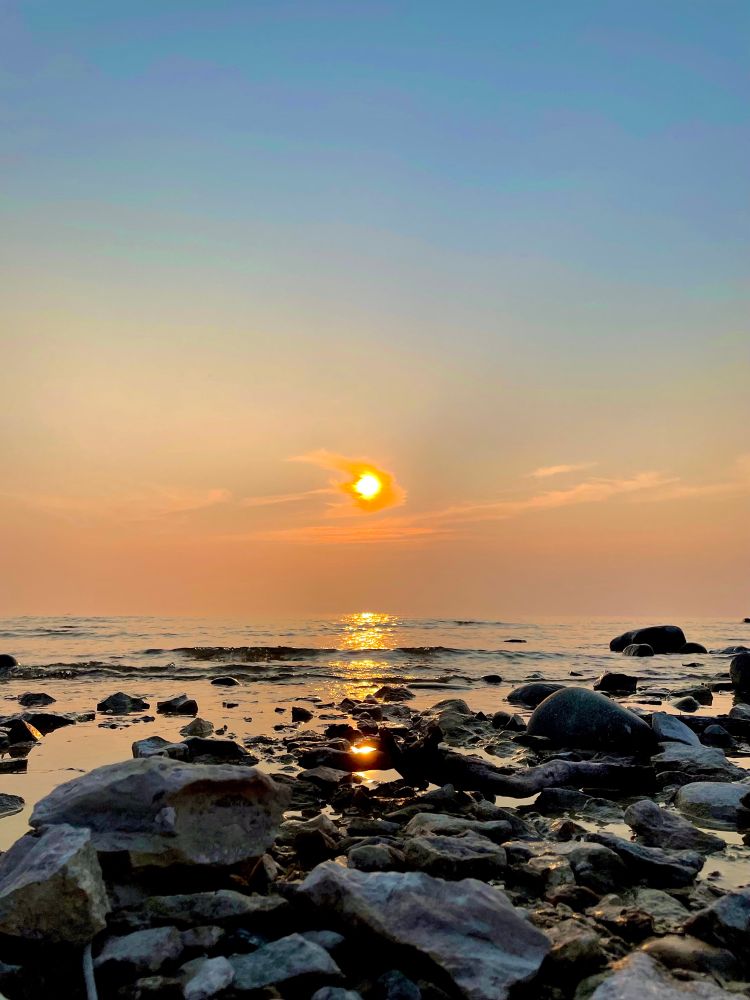 Sun setting on Lake Huron. Rocky shore in the foreground, calm water and blue/orange sky above