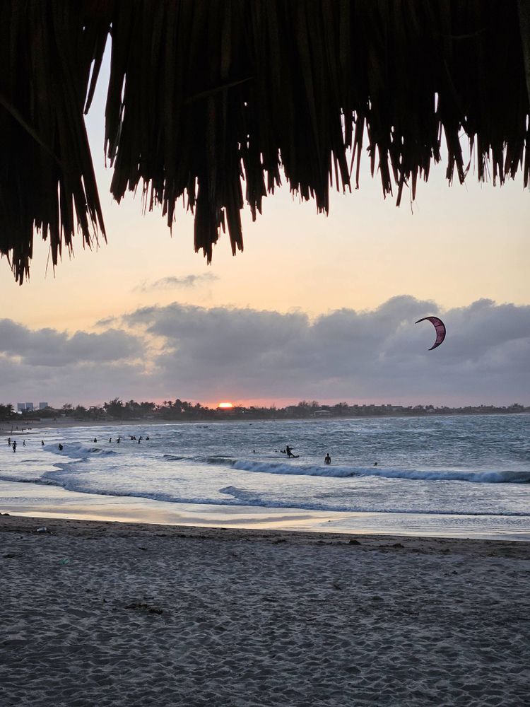 Praia ao por do sol com alguns banhistas e um kitesurf