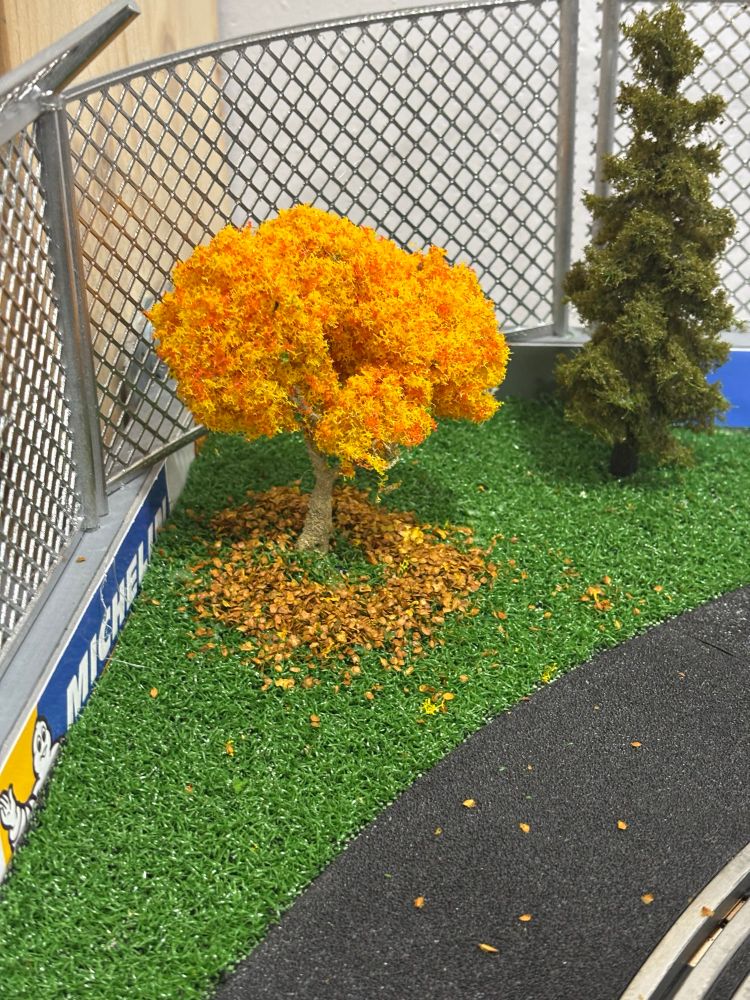 Arbol de una maqueta de slot scalextric con hojas amarillas caidas en el cesped.