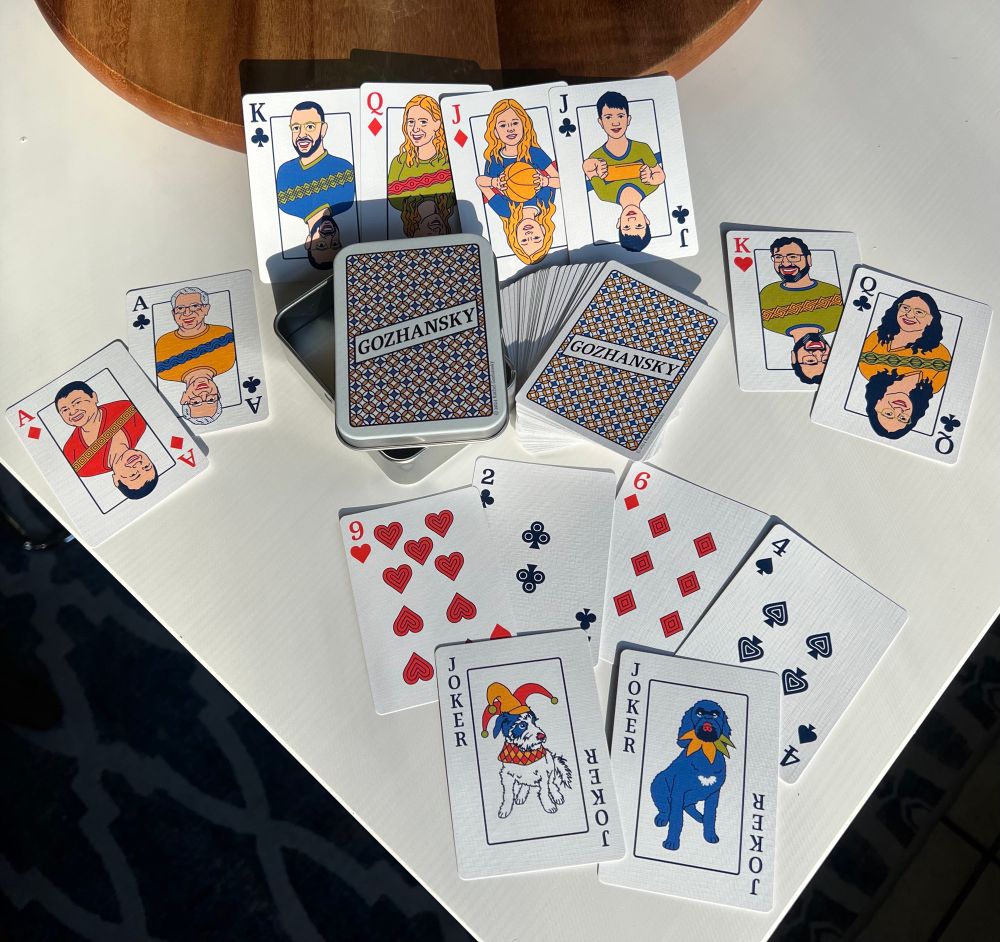 Photo of a custom illustrated card deck spread out to show the various card illustrations and designs. The art uses a limited color palette and vector illustration. Each face cards features an illustration of a member of the Gozhansky family. 