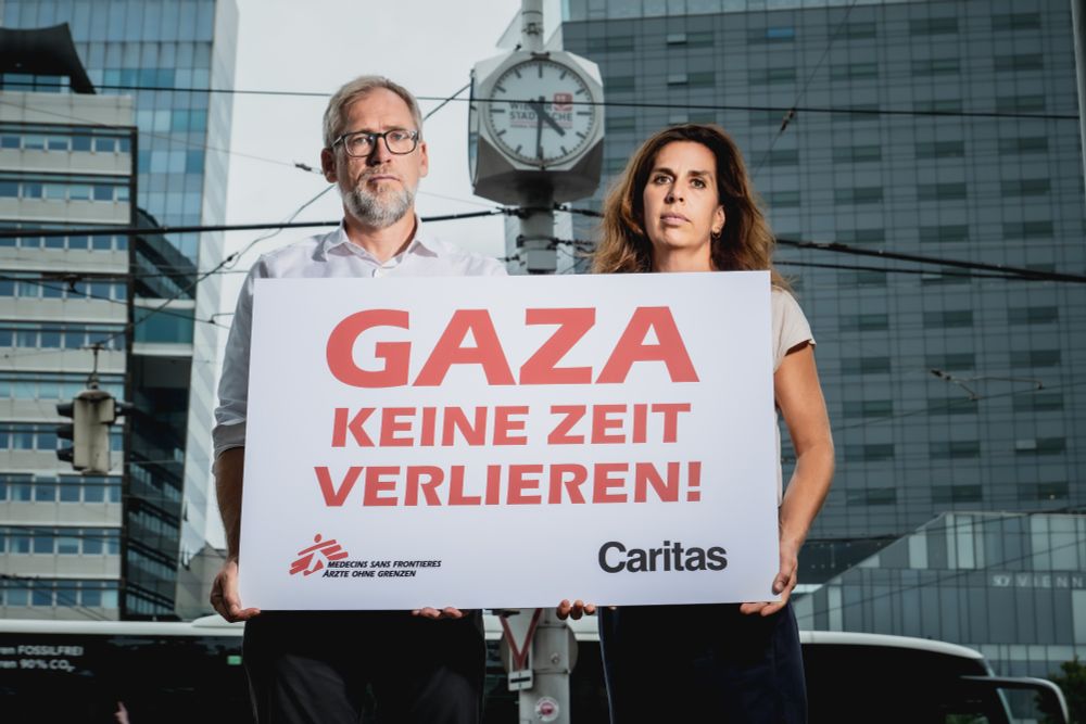 Alexander Bodmann, Vizepräsident der Caritas Österreich und Laura Leyser, Geschäftsführerin von Ärzte ohne Grenzen Österreich halten Schild mit Schriftzug "Gaza keine Zeit verlieren". Im Hintergrund eine Uhr
